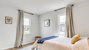 Une chambre à coucher avec un lit, une chaise, une fenêtre et deux tableaux encadrés accrochés au mur.
