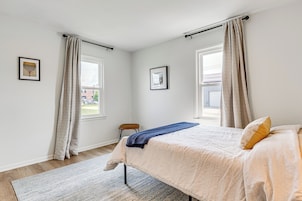 Un dormitorio con una cama, una silla, un ventanal y dos cuadros en la pared.