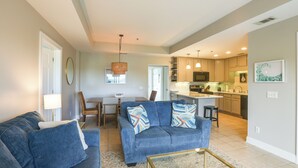 A modern living room with a blue sofa, a glass coffee table, and a dining area with a table and chairs.