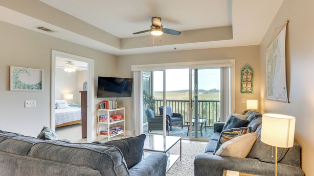 A living room with a sofa, a coffee table, a TV, a bookshelf, and a balcony with outdoor seating.