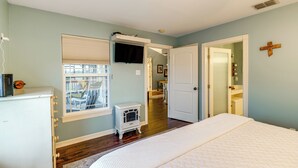 Ein Schlafzimmer mit einem großen Bett, einem Fernseher, einem Fenster mit Jalousien und einer Tür zu einem anderen Raum.