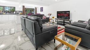 Un salon moderne avec un canapé en cuir noir, une table basse en verre et un téléviseur à écran plat diffusant Netflix.