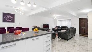 Un salon moderne avec un canapé en cuir noir, un coin repas doté d’un plan de travail noir et un téléviseur diffusant Netflix.