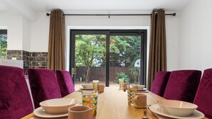 Un coin repas avec une table en bois dressée pour quatre personnes, des chaises à l’assise rembourrée de couleur violette et une vue sur le jardin à travers une porte vitrée.