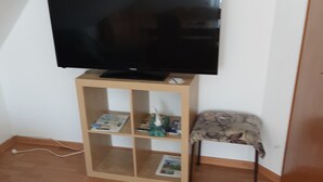Habitació amb televisió sobre un suport de fusta, una cadira petita i un terra de fusta.