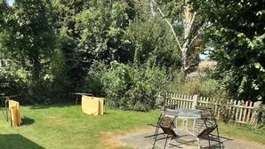 Un pati enjardinat amb taula i cadires de picnic, envoltat d'arbres i una tanca de fusta.