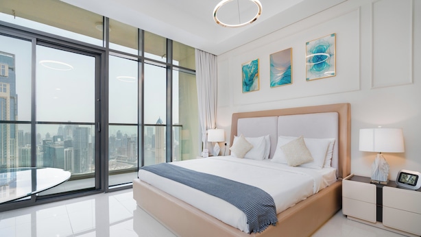 A modern hotel room with a large bed, two bedside tables, and a city view through floor-to-ceiling windows. - Lux BnB Aykon City I Skyline Canal Views (Dubai)