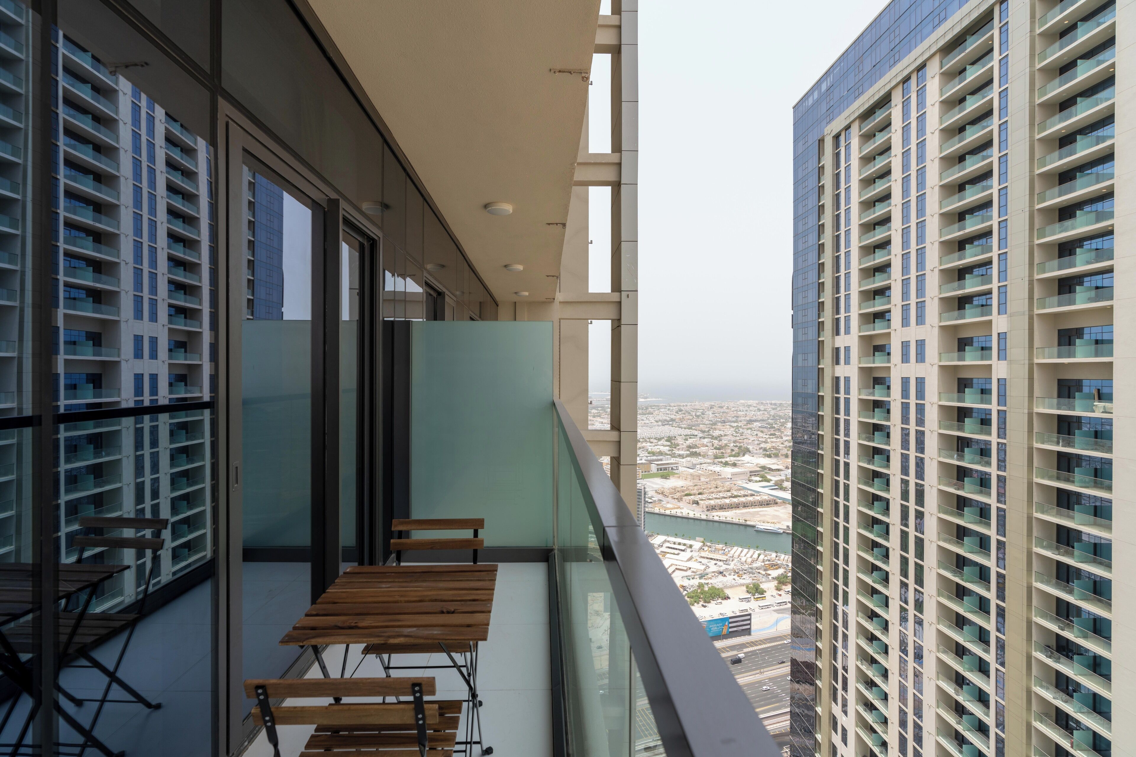 A balcony with a table and chairs, overlooking a cityscape and a body of water.