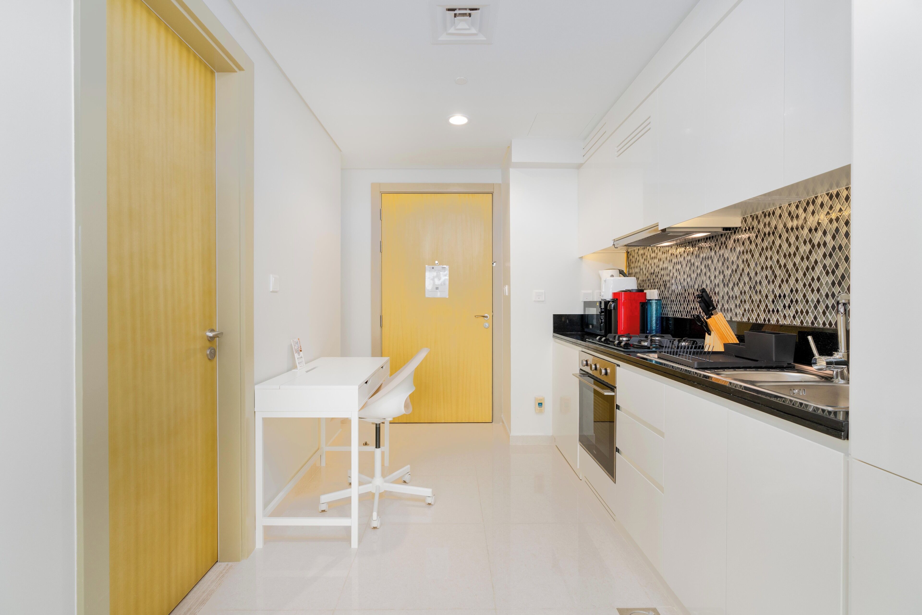 A modern kitchen with white cabinets, a wooden door, and a countertop with various appliances.