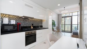 A modern kitchen with white cabinets, a black countertop, and stainless steel appliances. There is a dining area with a white table and chairs. - Lux BnB Aykon City I Skyline Canal Views (Dubai)