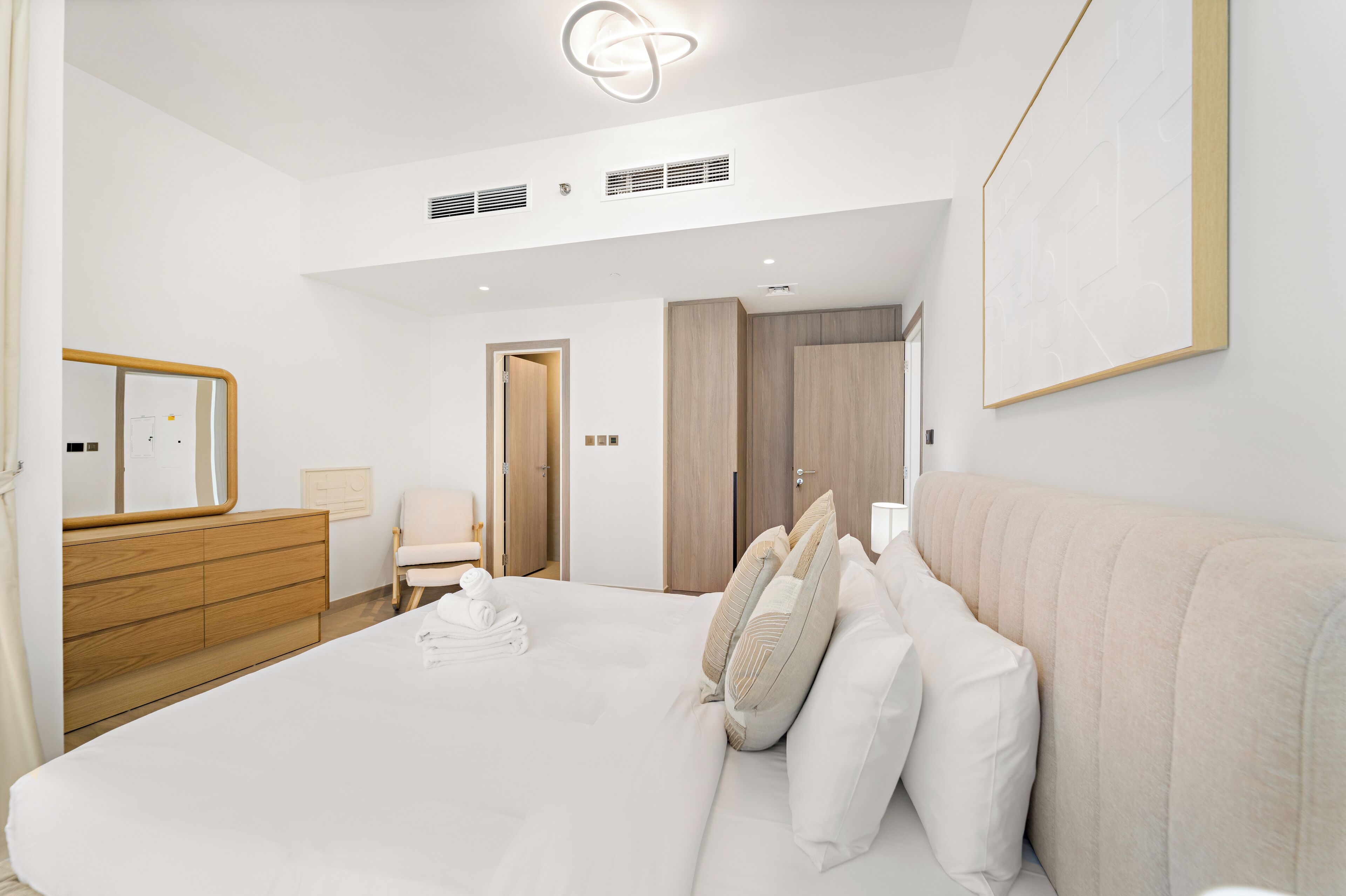A modern hotel room with a large bed, a wooden dresser, a chair, and a framed picture on the wall.
