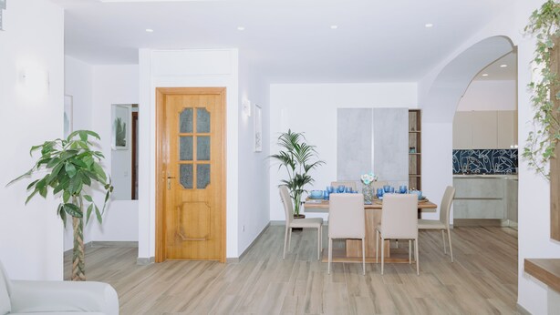 Un espace repas moderne avec une porte en bois, une table à manger avec des chaises, et une cuisine visible à travers une arche.