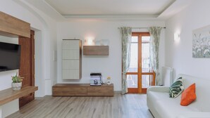 Un salon moderne avec un canapé blanc, un banc en bois, un aquarium et un téléviseur fixé au mur.