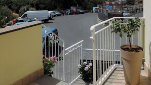 Un balcon donnant sur un parking, avec une plante en pot et une rambarde.