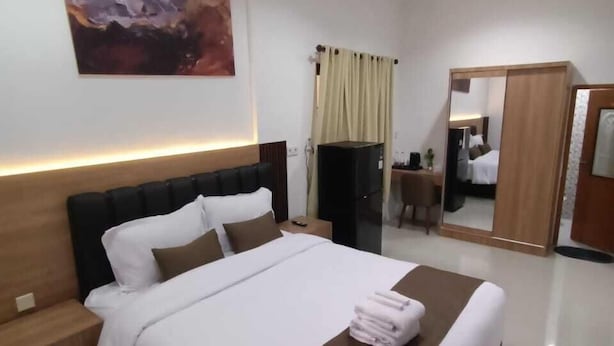 Une chambre d’hôtel moderne avec un grand lit, une table de chevet, une commode, un miroir et un tableau au mur.