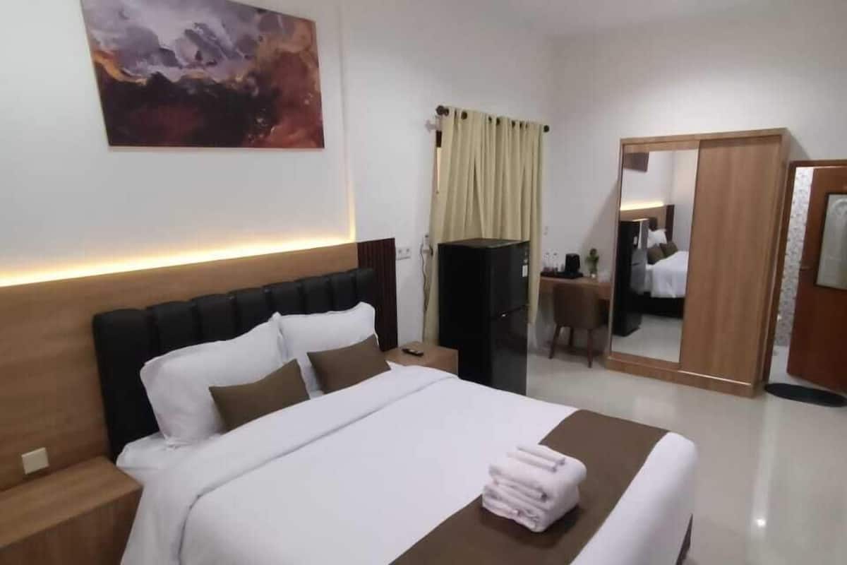 A modern hotel room with a large bed, a bedside table, a nightstand, a mirror, and a painting on the wall.