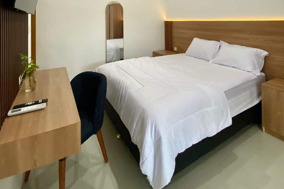 A modern hotel room with a bed, a desk, a chair, a TV, and a mirror.