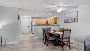 A modern kitchen with wooden cabinets, a dining area with a table and chairs, and a ceiling fan. - 1013 - Coastal Haven Retreat (Westport)
