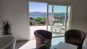 A room with two armchairs and a small table, a sliding glass door leading to an outdoor area with a view of mountains and greenery. - HOTEL BORGO DELL'ORSO (Palau)