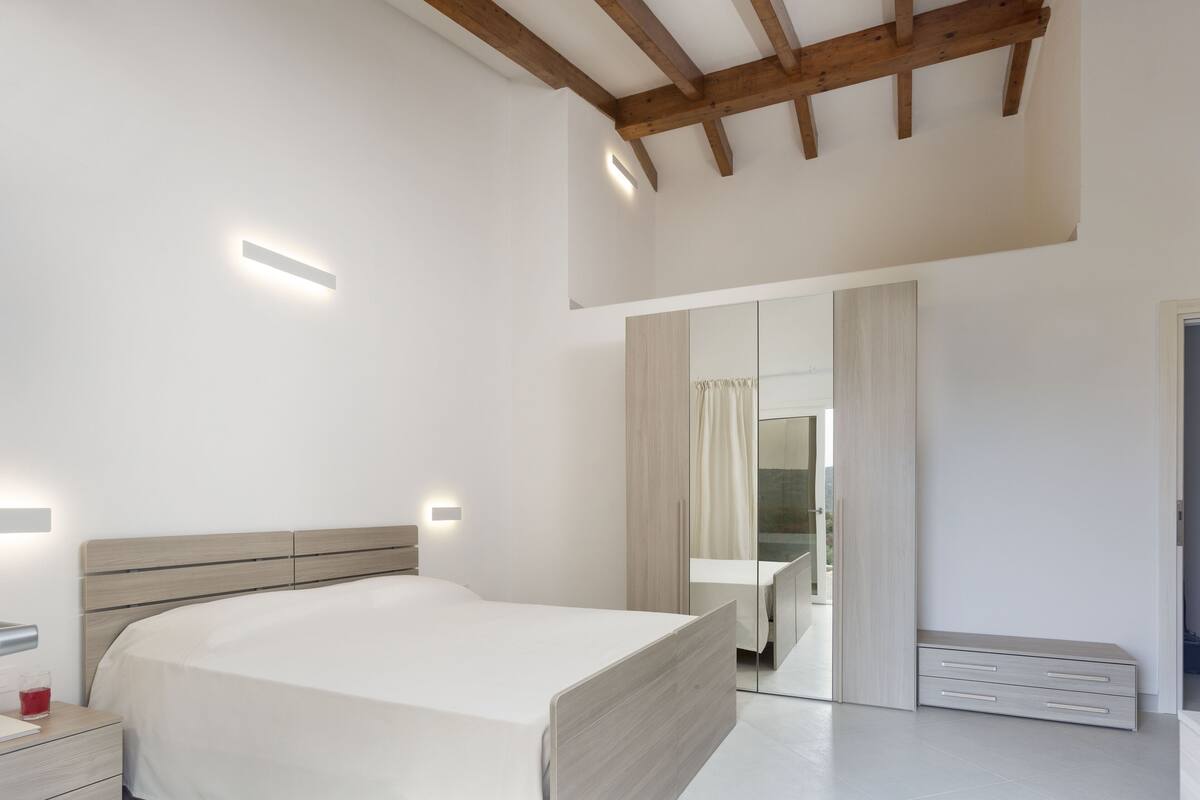 A modern bedroom with a wooden ceiling, a bed with a wooden headboard, a bedside table, and a mirror.