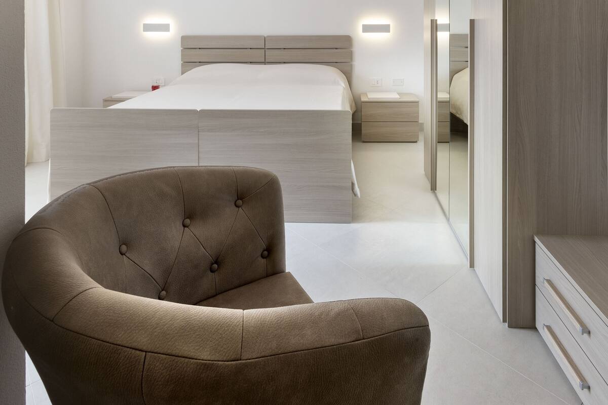 A modern bedroom with a bed, bedside tables, a chair, and built-in wardrobes.