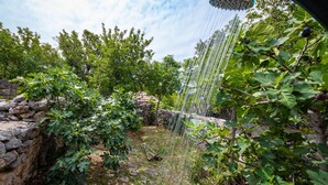Un jardín con muro de piedra, higueras y una fuente de agua.