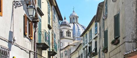 A narrow street with historic buildings, a prominent dome structure in the background, and a car parked on the side.
