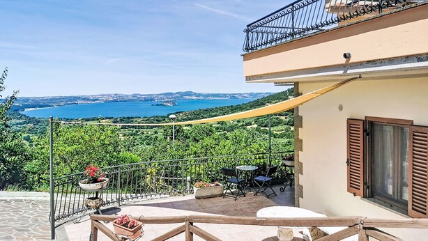 A balcony with a view of a coastal landscape, a table with chairs, and a potted plant. - Casa Martina by Interhome (Lago di Bolsena)