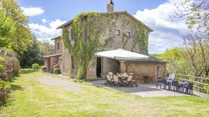 A stone building with ivy-covered walls, a patio with outdoor furniture, and a gravel path leading to the entrance. - Casale Vitello by Interhome (Lago di Bolsena)