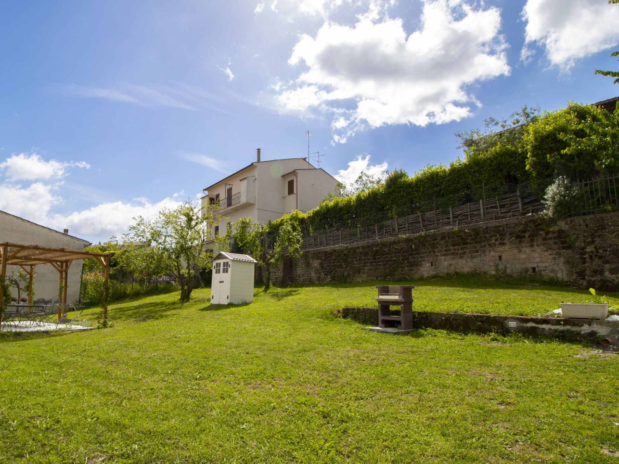 A grassy yard with a small shed, a wooden bench, and a stone wall.