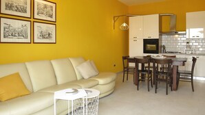 Un salon moderne avec un canapé et une table à manger, une cuisine avec des meubles blancs et des tableaux encadrés au mur.
