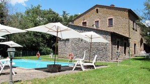 A stone building with a swimming pool, white umbrellas, and lounge chairs. - La Capraccia (BOL334) by Interhome (Lago di Bolsena)