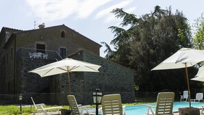 A stone building with a pool area, outdoor seating, and umbrellas.