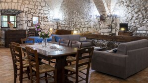A rustic stone-walled room with a dining table, chairs, a sofa, and a television. - La Capraccia by Interhome (Lago di Bolsena)