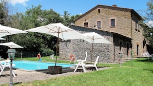Un edificio de piedra con piscina, sombrillas blancas y sillones de descanso.