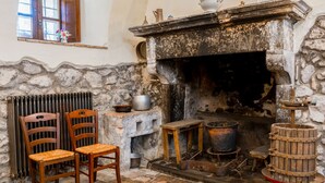 Una cocina rústica con chimenea de piedra, sillas de madera, un radiador y diversos utensilios de cocina.