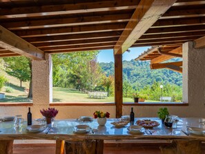 An outdoor dining area with a wooden table set for a meal, overlooking a lush landscape with trees and hills. - Podere Le Ripe by Interhome (Vicchio)