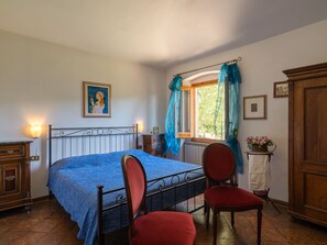 A bedroom with a bed, two chairs, a dresser, a window with curtains, and a radiator. - Podere Le Ripe by Interhome (Vicchio)