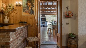 Ambiente rustico con un bancone in legno, un quadro, un camino e vista su un patio esterno.