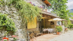 Una casa de pedra amb un porxo cobert, mobiliari exterior i una paret de pedra amb plantes enfilades.