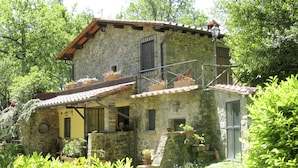 Una casa de pedra amb un balcó, envoltada de verdura abundant.