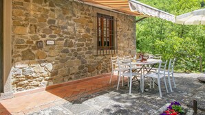 A stone building with a tiled patio, outdoor seating, and a view of a forested hill. - La Fornace by Interhome (Loro Ciuffenna)