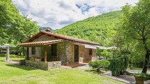 A stone cottage with a tiled roof, surrounded by lush greenery and a mountainous backdrop. - La Fornace by Interhome (Loro Ciuffenna)