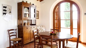 Uma área de refeições com uma mesa e cadeiras de madeira, um armário com portas de vidro e uma janela com design em arco.