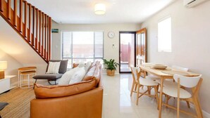 A modern living room with a brown leather sofa, a dining table with chairs, a staircase, and a large window with blinds. - Sunsets on Hampton, walk to central Fremantle. Free parking and wifi. (Fremantle)