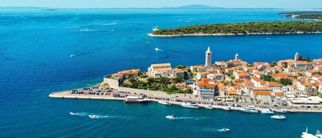 An aerial view of a coastal town with a prominent tower, a marina with boats, and a small island with dense greenery.