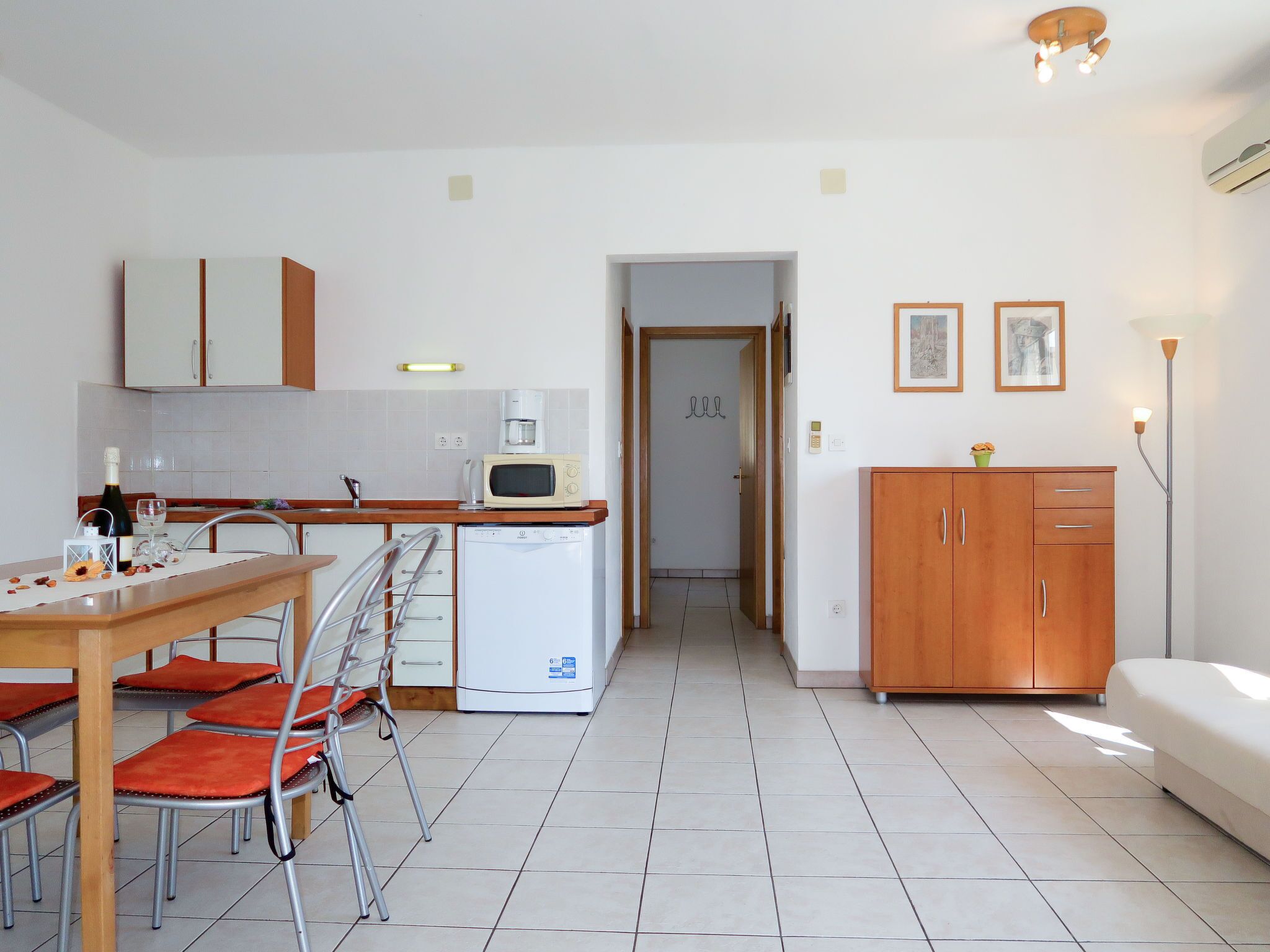 Cocina compacta con microondas, cafetera y refrigerador pequeño. Hay una mesa de comedor con sillas y un sofá en la sala.