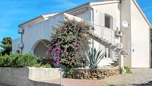 Un edificio a due piani con un balcone, un'antenna parabolica e un muro in pietra.