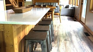 A wooden interior with a kitchen area, bar stools, a sofa, and a ceiling fan.