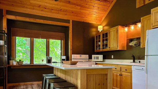 A modern kitchen with wooden cabinets, a central island with stools, a microwave, a stove, and a dishwasher.